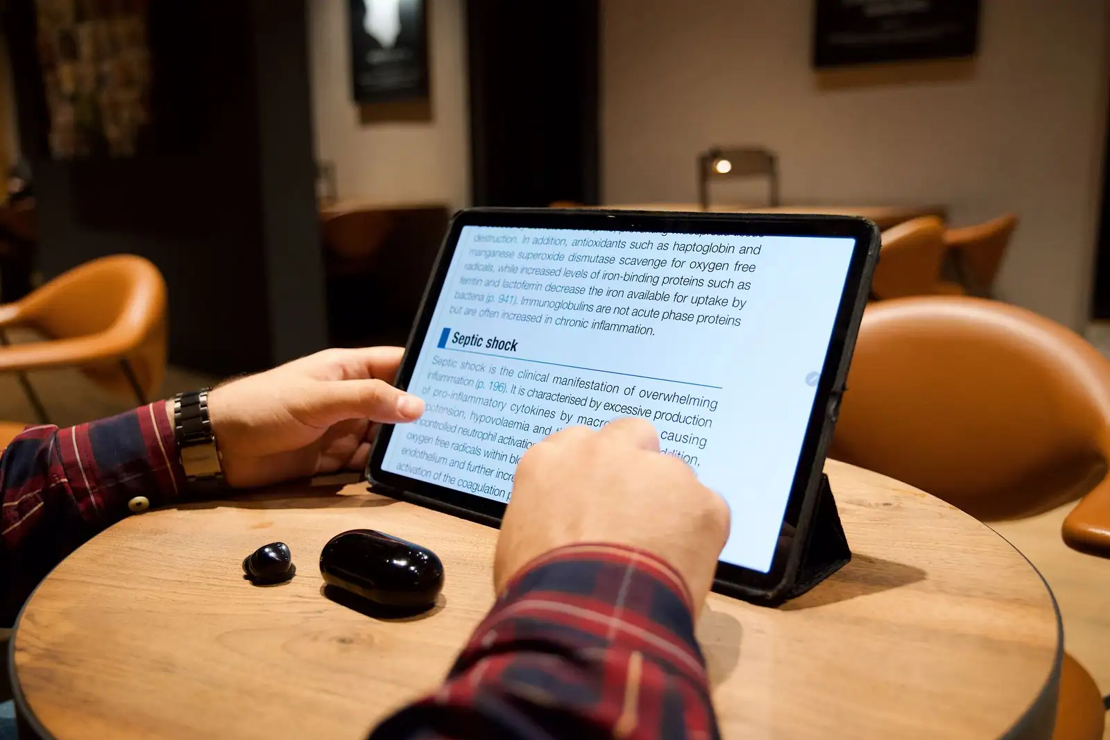 Personne lisant un texte sur l'écran d'une tablette posée sur une table, dans un lieu public.