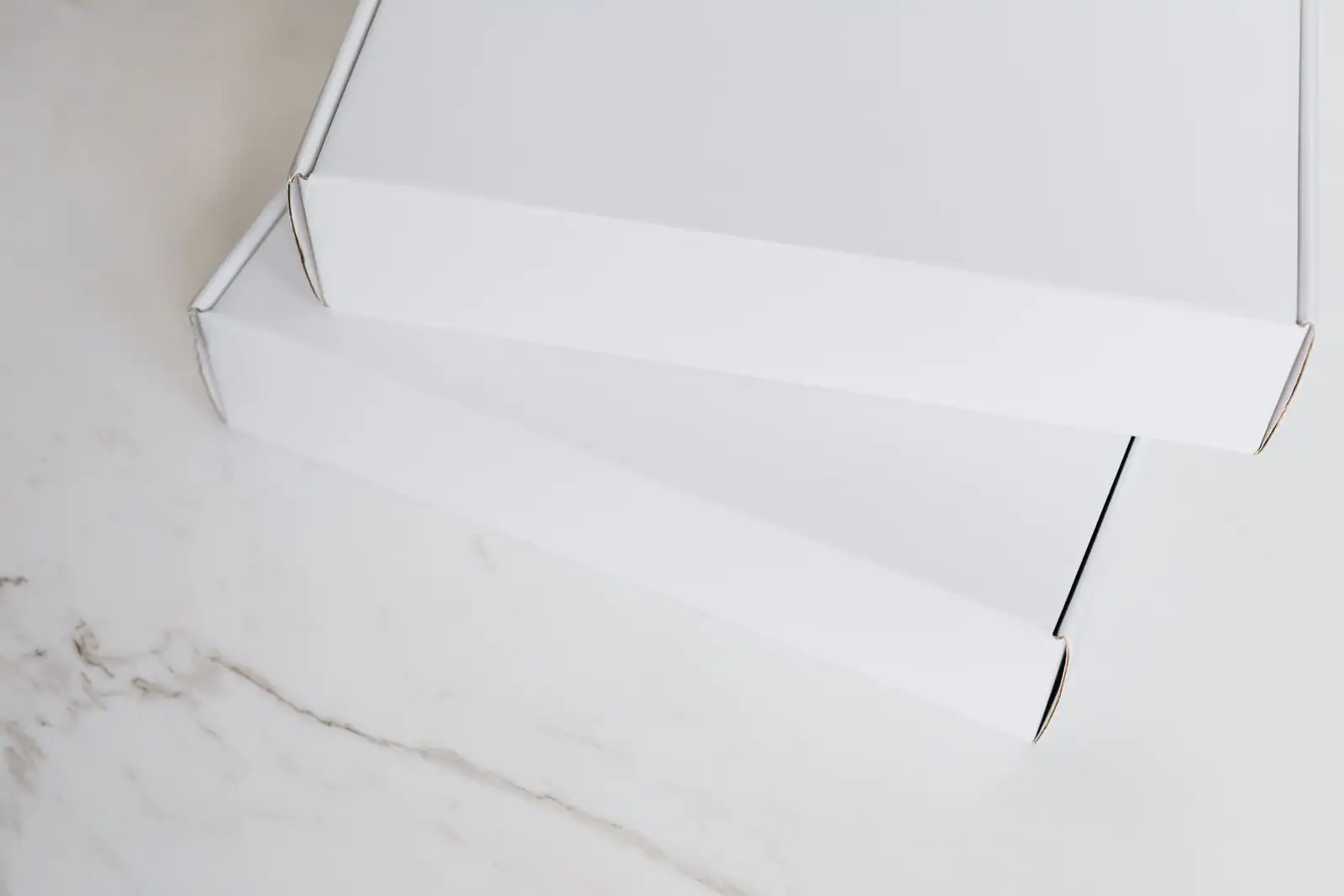Deux boîtes d'expédition en carton blanc fermées, posées sur une surface claire, prêtes à l'envoi.