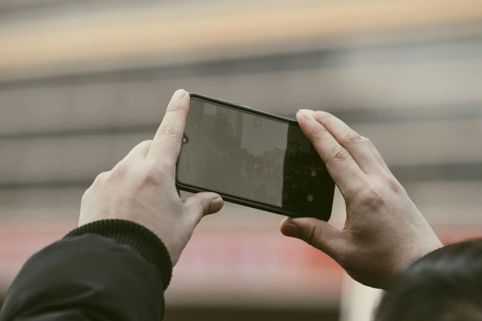 Personne tenant un smartphone à deux mains en extérieur, application mobile à l'écran.