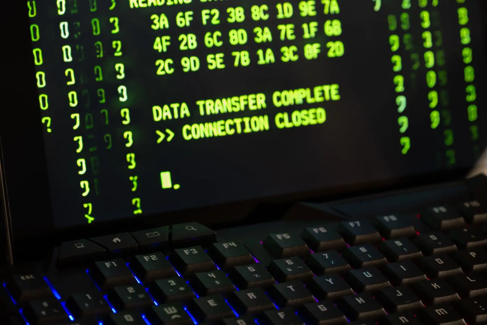 Écran affichant du code vert et un message de transfert de données, au-dessus d'un clavier rétroéclairé.