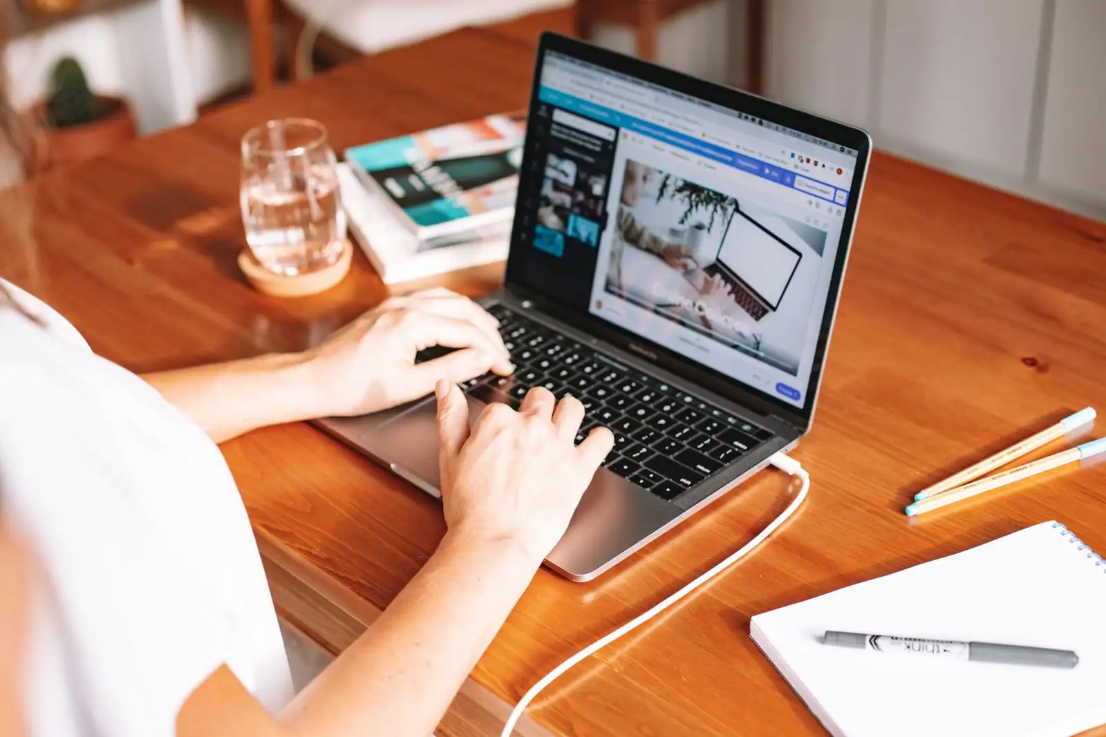 Personne en train de taper sur un ordinateur portable posé sur un bureau en bois