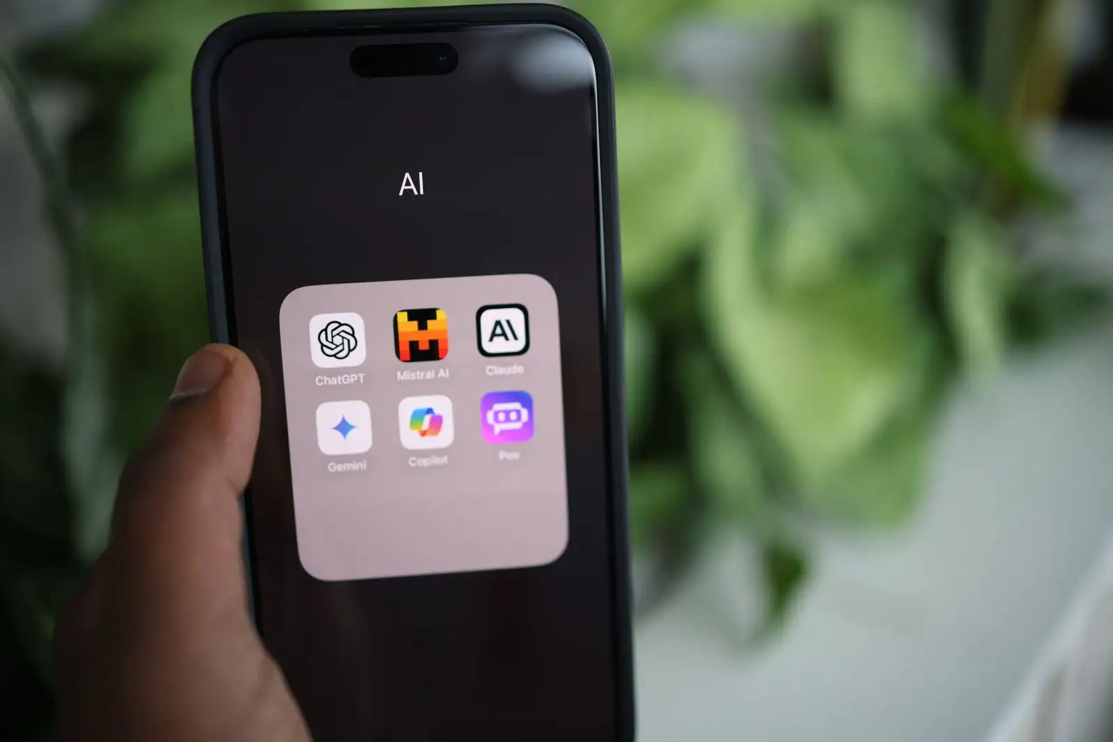 Smartphone tenu en main affichant un dossier d'applications d'IA, dont l'icône de ChatGPT