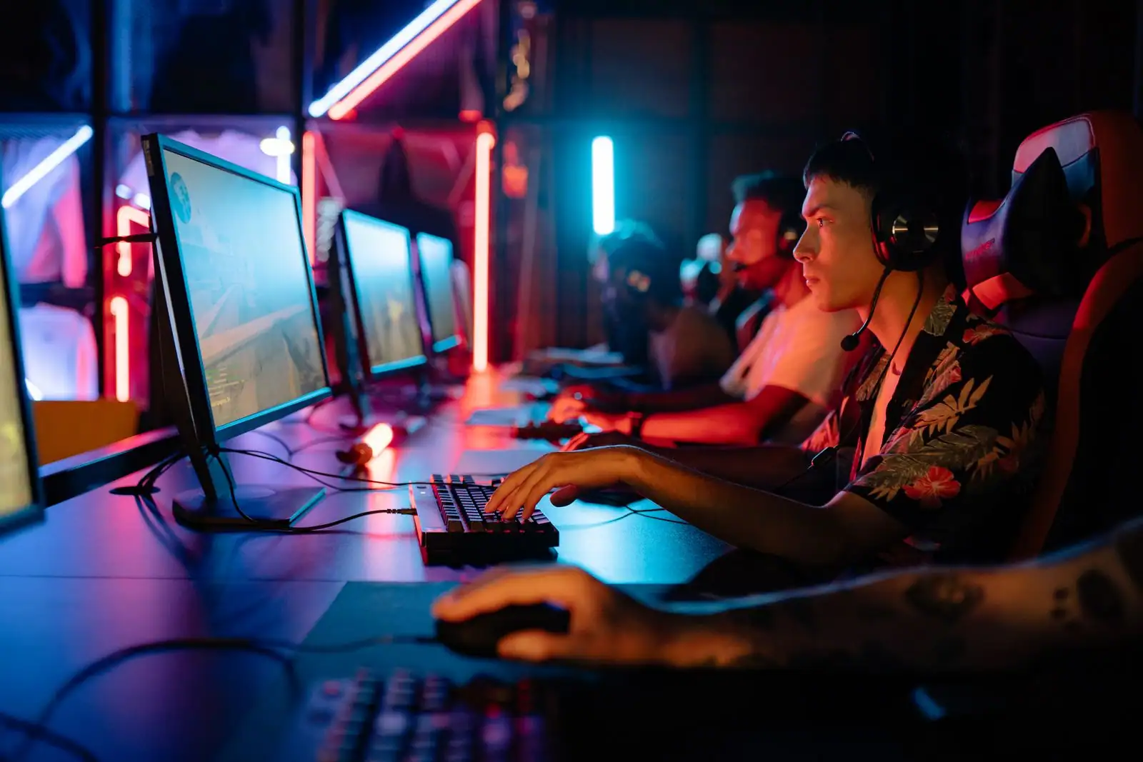 Joueurs équipés de casques alignés devant leurs ordinateurs dans une salle de jeu aux néons