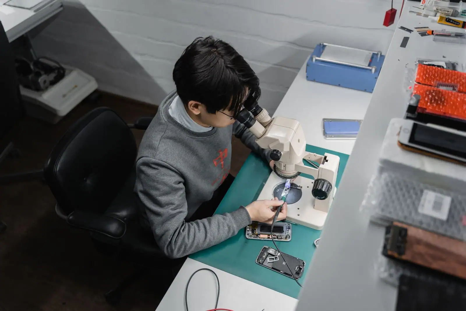 Technicien penché sur un microscope d'atelier pour réparer un smartphone démonté, entouré de pièces détachées.
