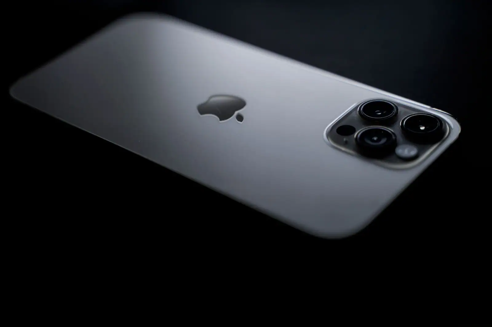 Dos d'un iPhone Pro récent au châssis clair et son bloc à trois objectifs, sur fond noir.