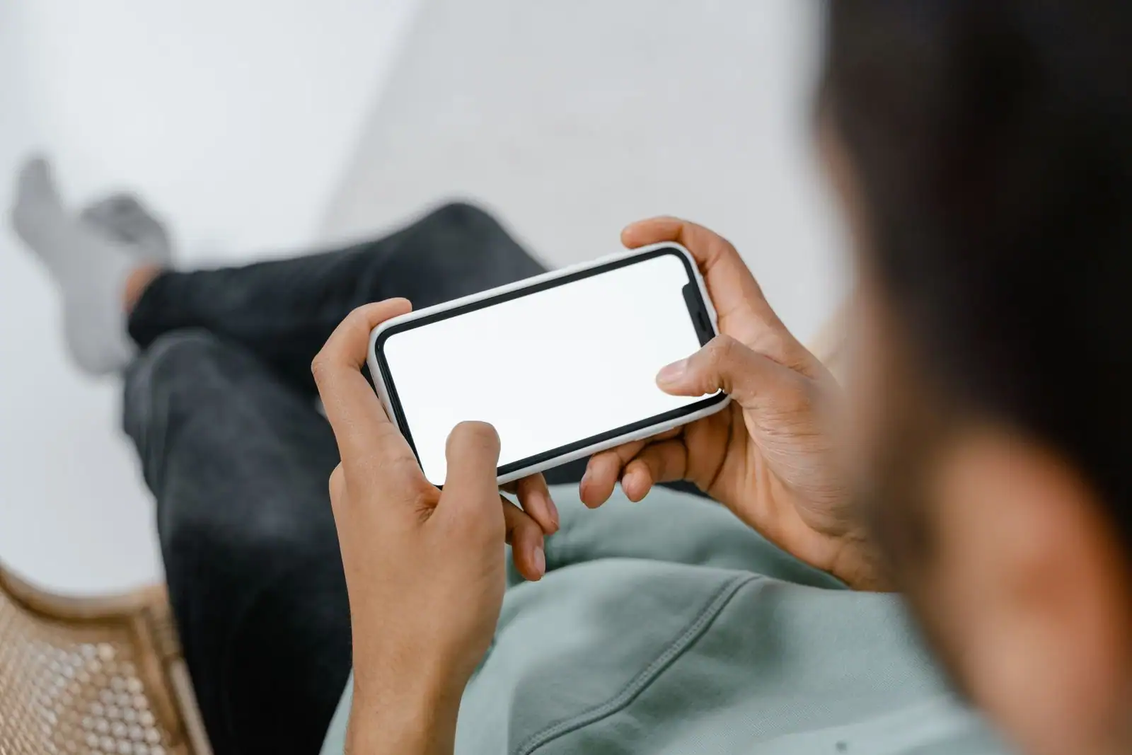 Personne assise tenant un smartphone à deux mains, l'écran vierge, vue par-dessus l'épaule.