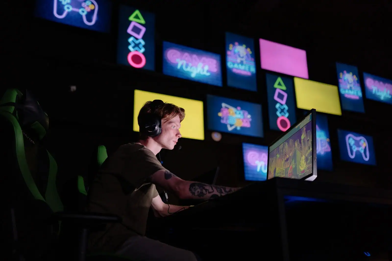 Jeune joueur avec un casque, concentré devant son écran dans un espace de jeu aux néons colorés.