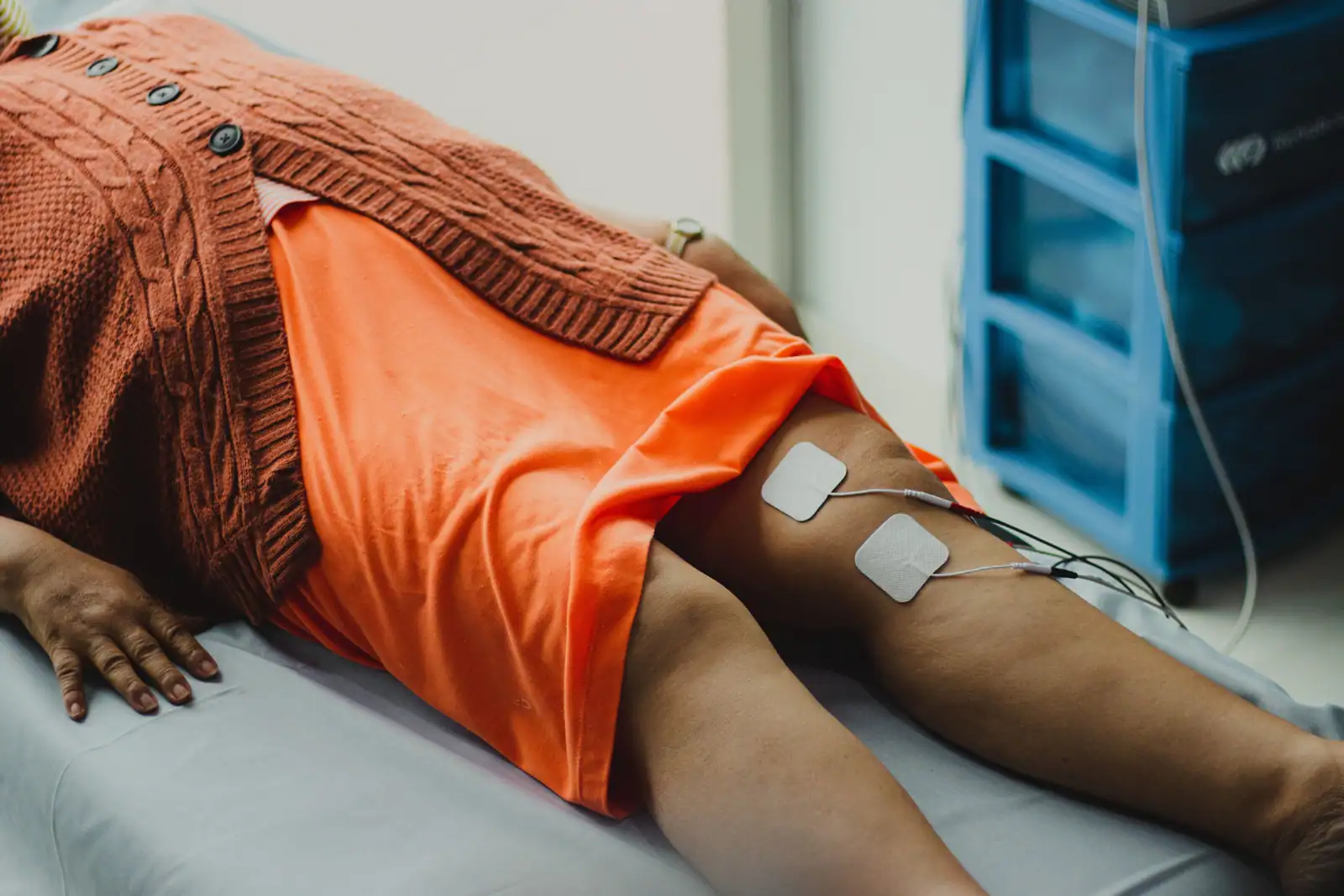 Électrodes de rééducation posées sur le genou d'un patient allongé lors d'une séance de physiothérapie.
