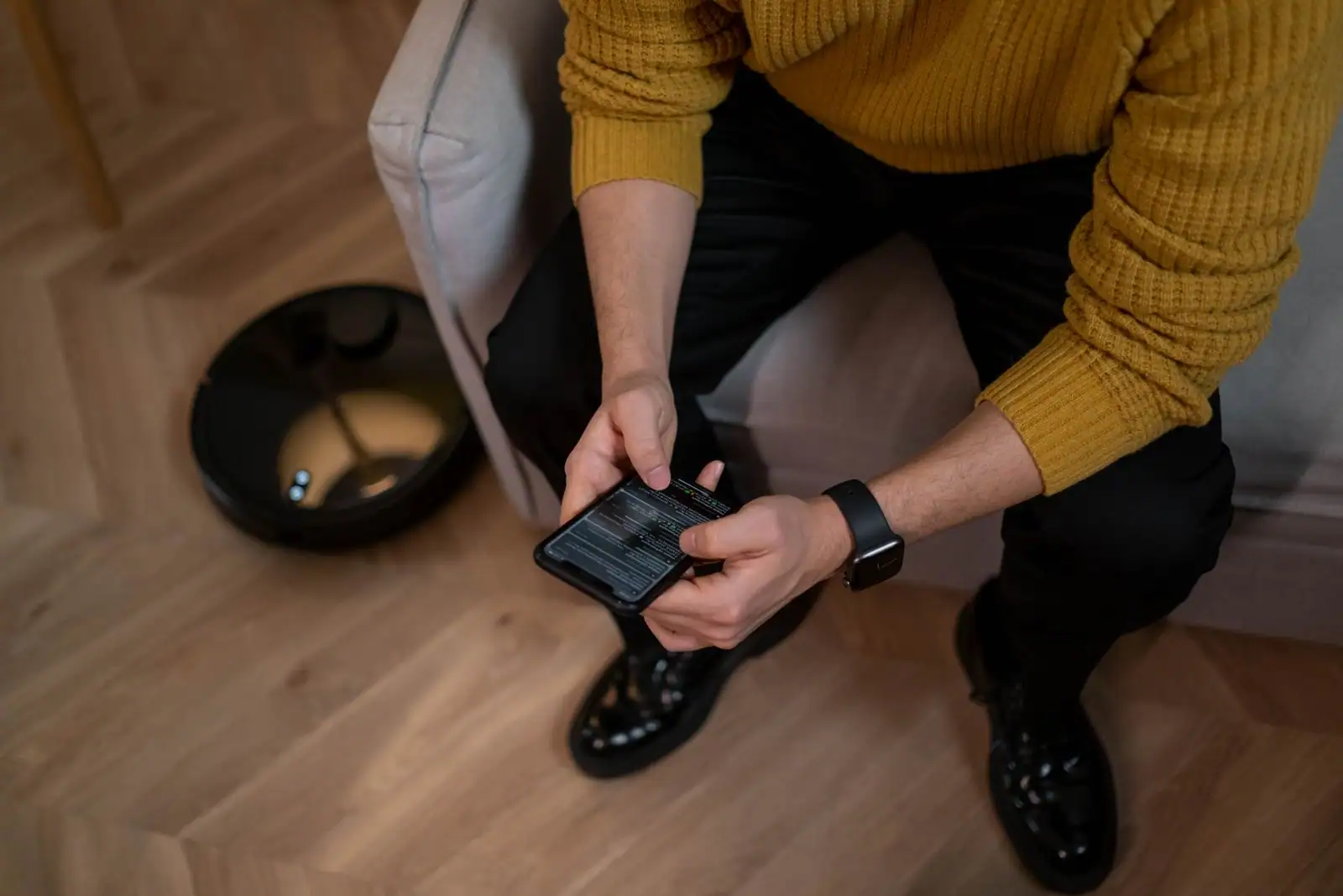 Personne réglant un aspirateur robot connecté depuis l'application de son smartphone.