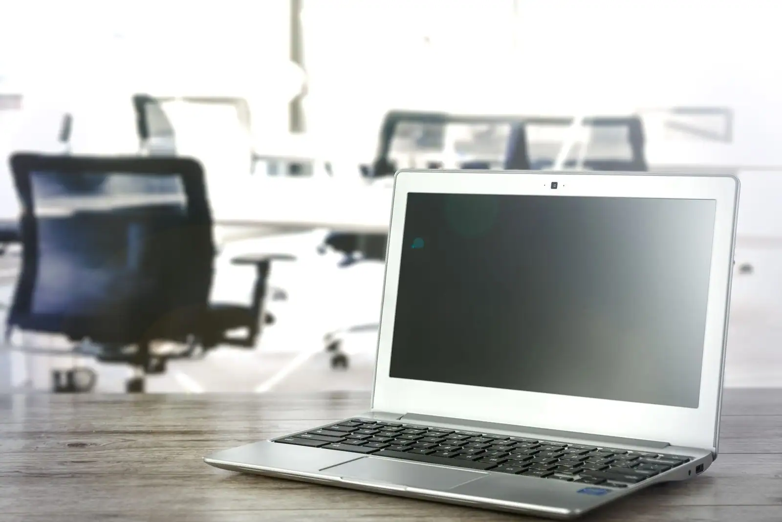 Ordinateur portable argenté ouvert sur un bureau, espace de travail flou en arrière-plan.