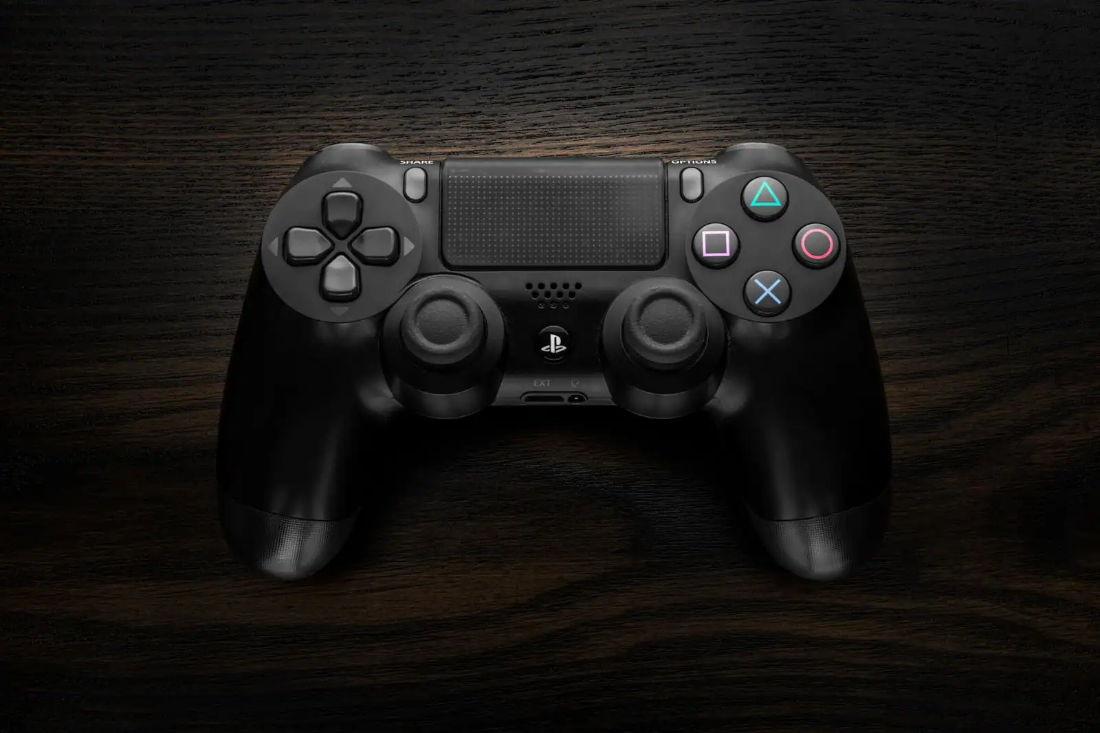 Manette de jeu PlayStation noire posée sur un plan de travail en bois sombre, vue de dessus.