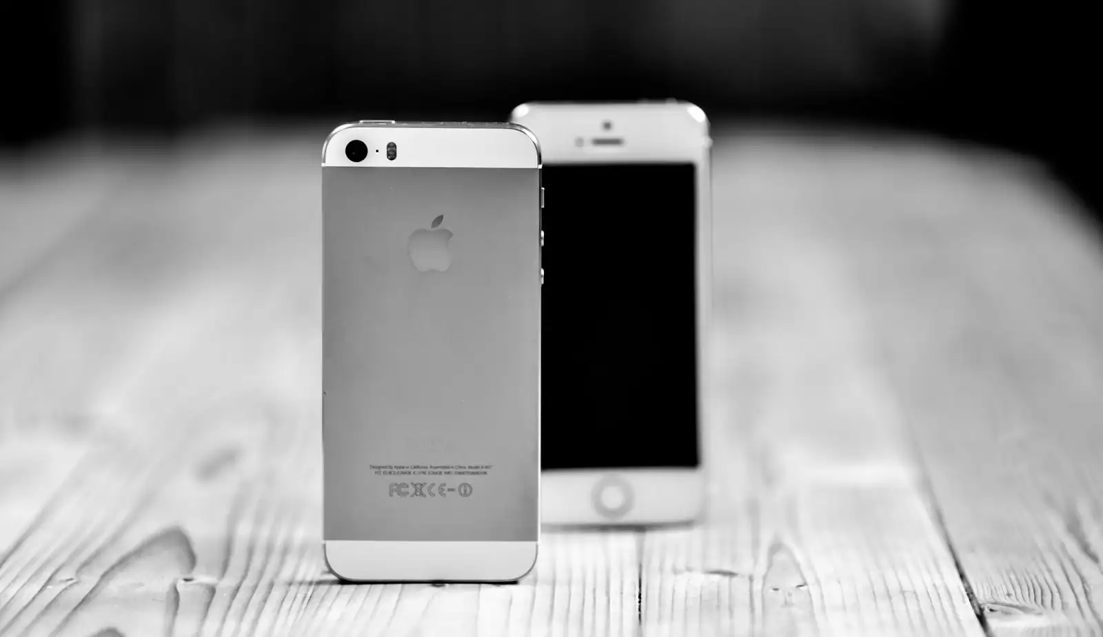 Deux smartphones posés côte à côte sur une surface en bois, l'un de dos, l'autre de face écran éteint.