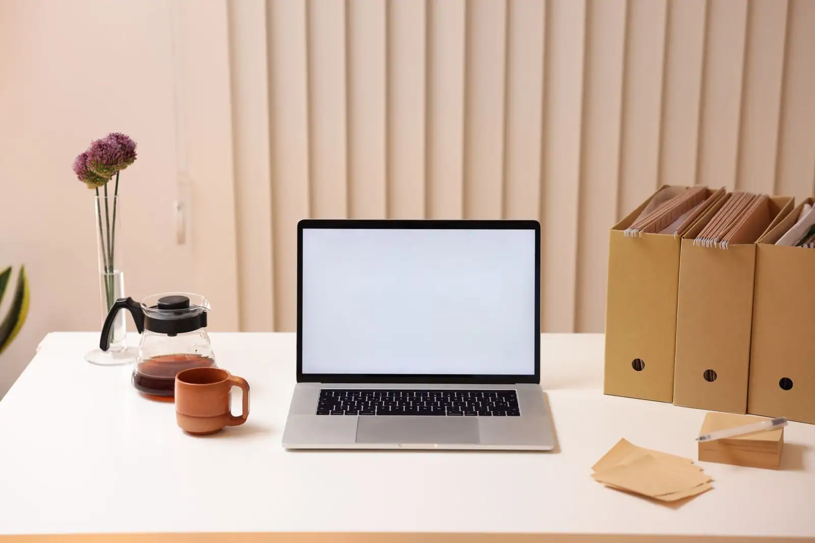 Ordinateur portable à l'écran vierge sur un bureau clair, à côté de boîtes de rangement de documents.