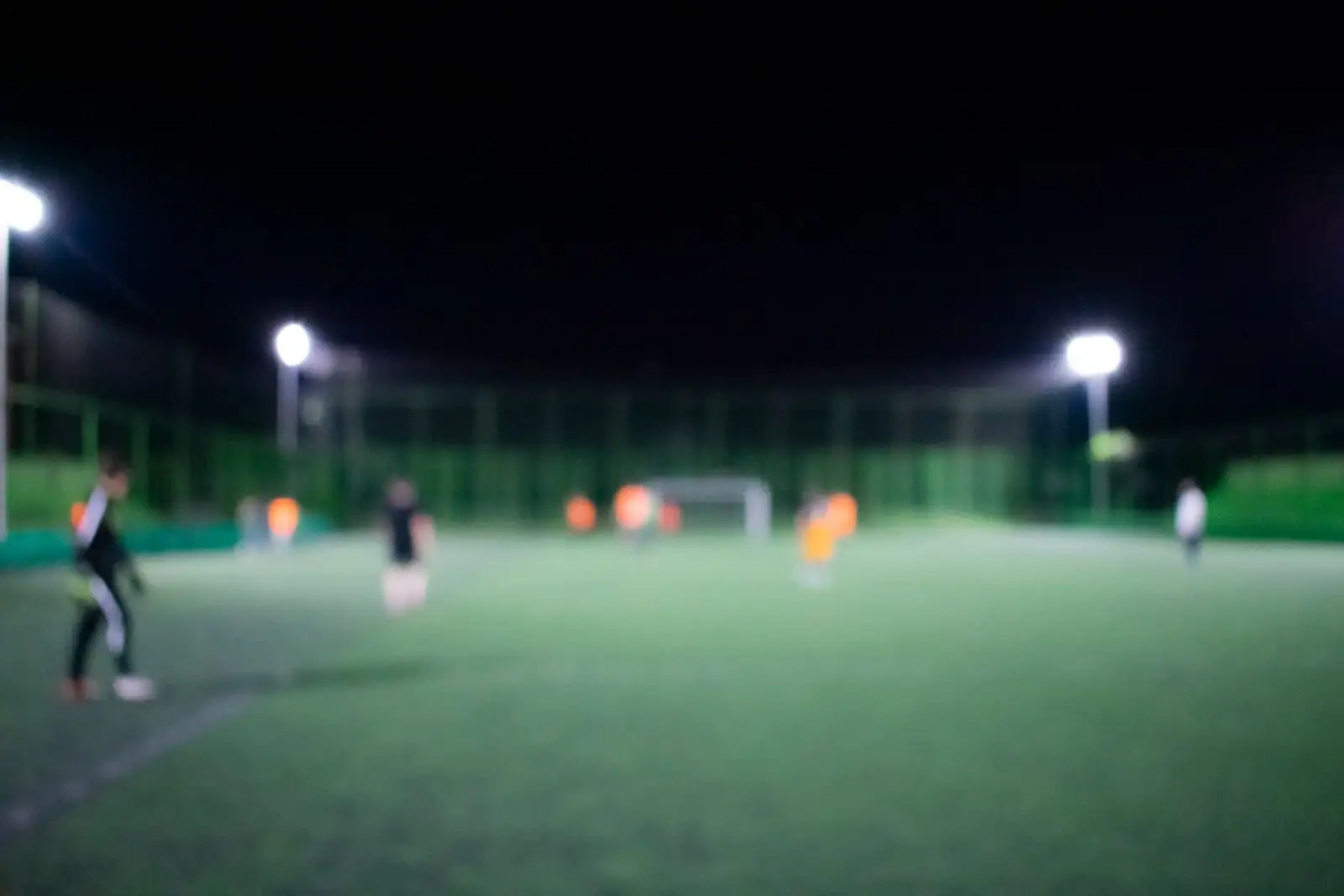 Terrain de football éclairé la nuit sous les projecteurs, des joueurs sur la pelouse verte.