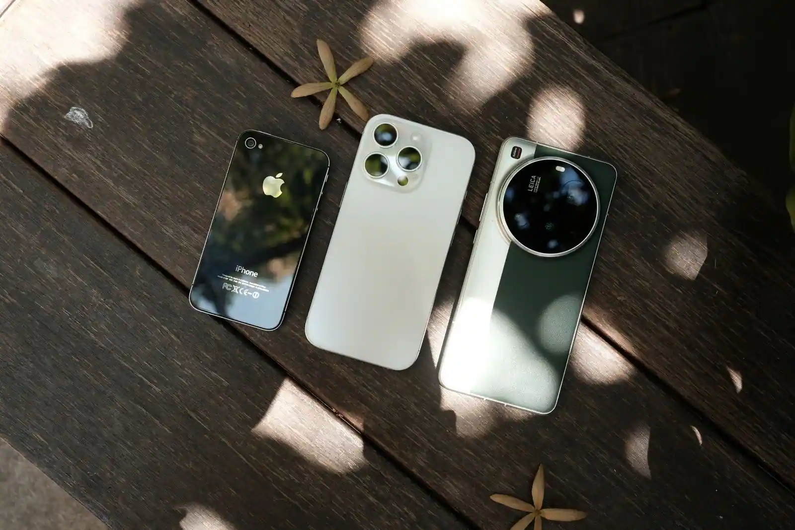 Trois smartphones de marques différentes posés côte à côte sur une table en bois, vus de dos pour comparaison.
