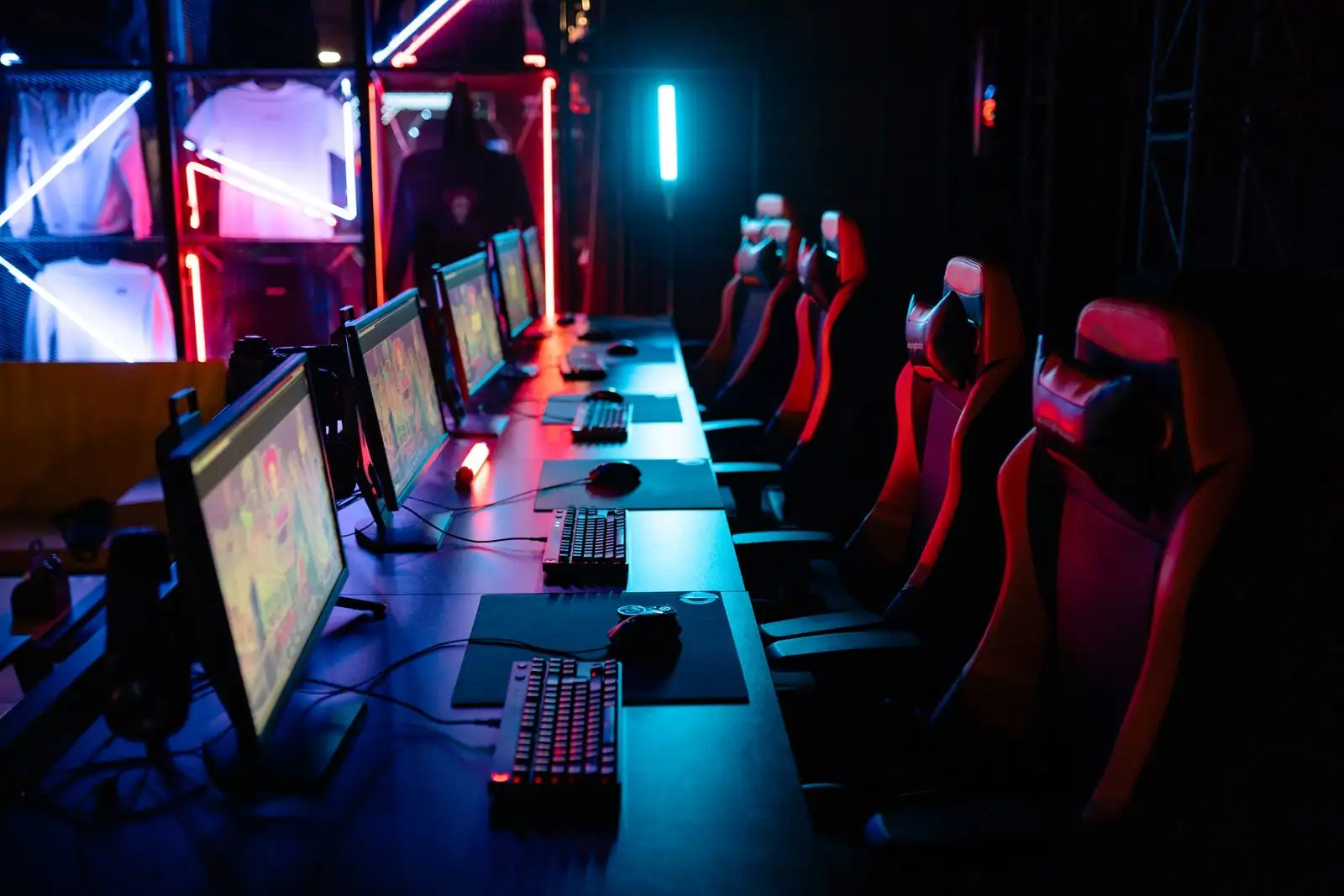 Salle d'esport avec une rangée d'écrans de jeu et des fauteuils gaming sous un éclairage néon.