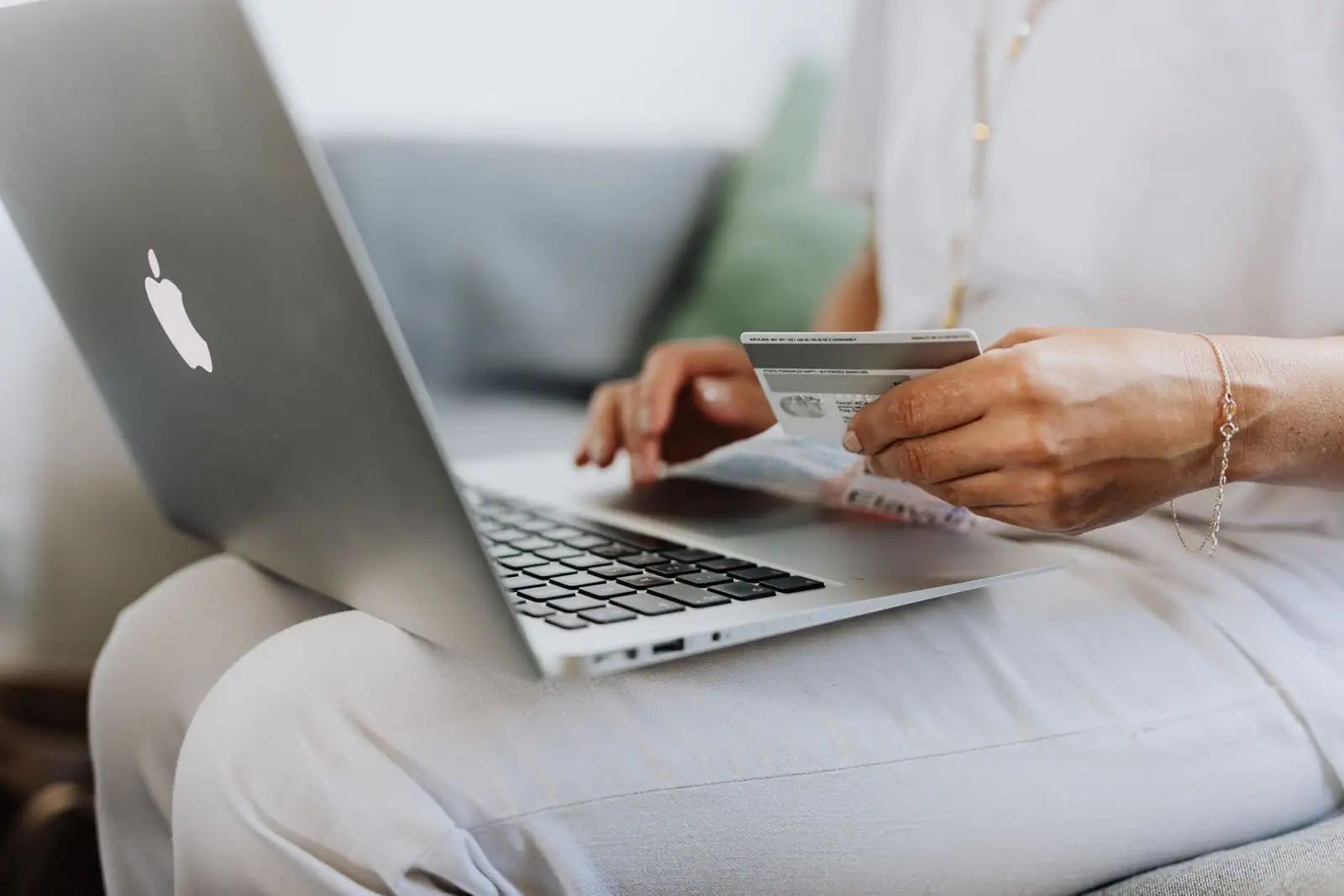 Personne tenant une carte bancaire devant un ordinateur portable pour un achat en ligne.