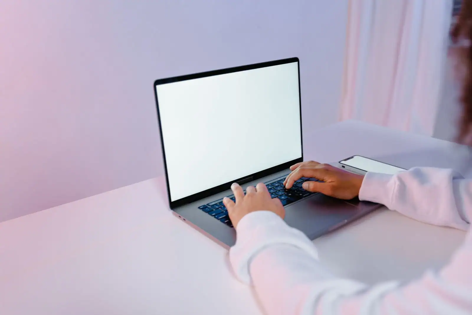 Personne tapant sur un ordinateur portable à l'écran vierge, un smartphone posé à côté sur un bureau clair