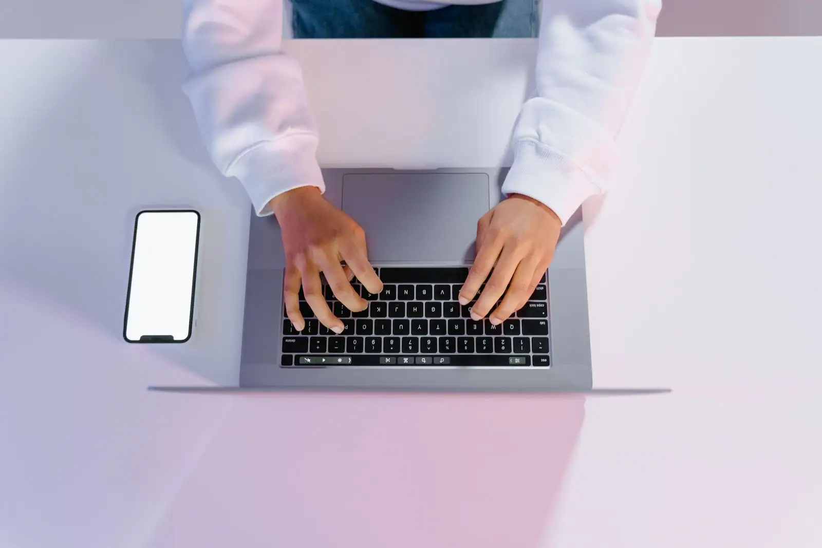 Mains tapant sur un ordinateur portable, un smartphone posé à côté sur un bureau clair