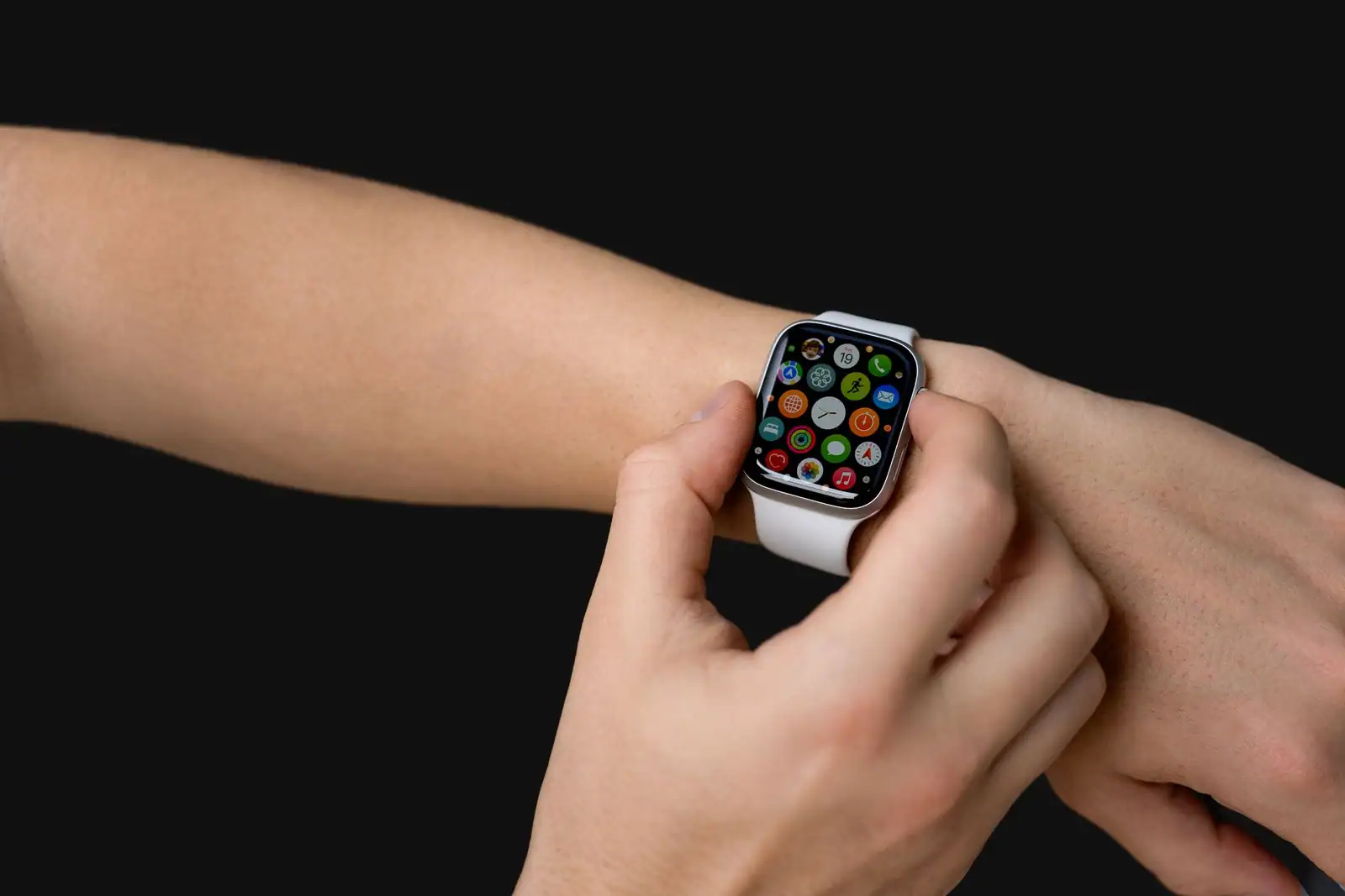 Mains posées sur une montre connectée rectangulaire au poignet, écran affichant une grille d'icônes colorées