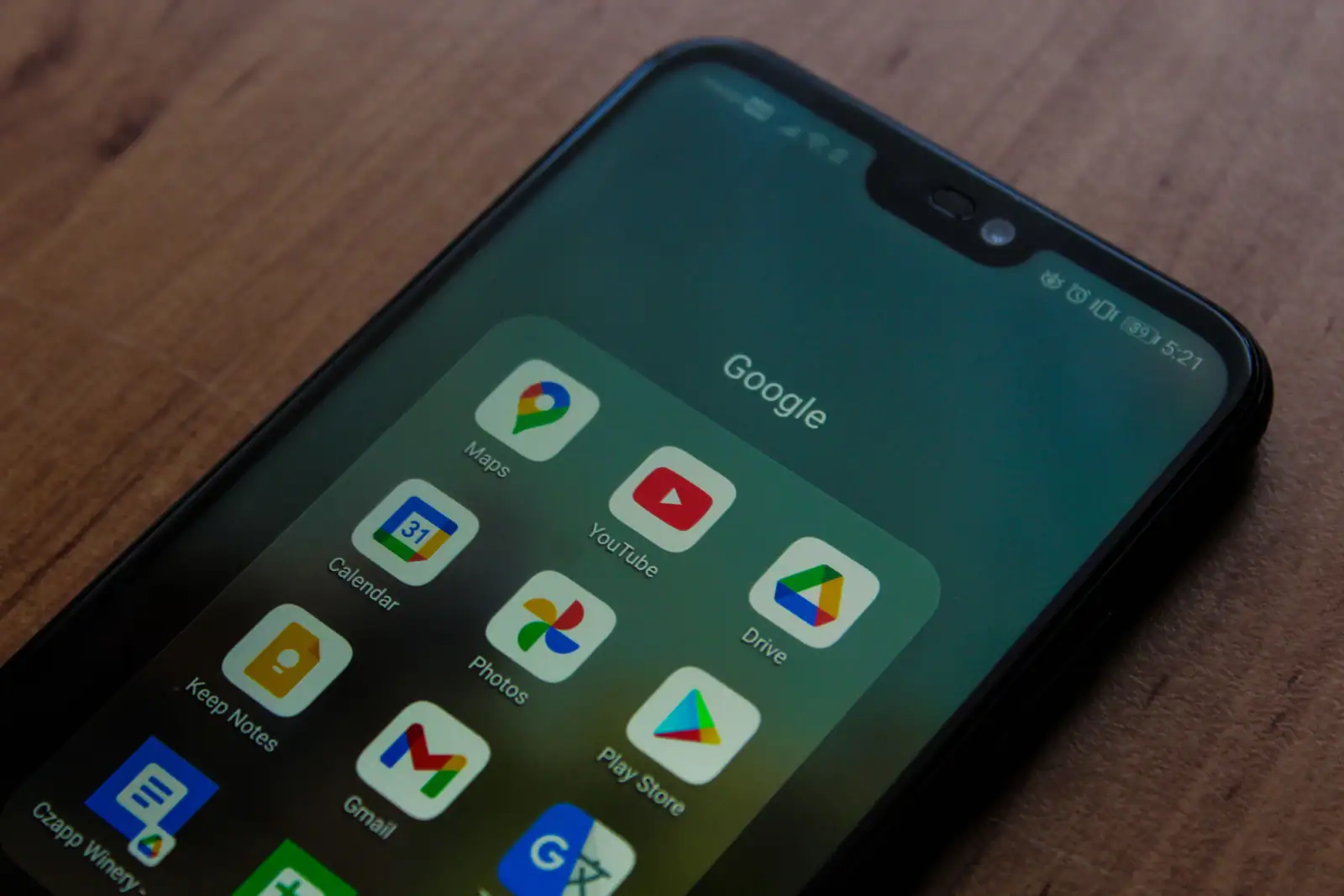 Écran d'un smartphone Android posé sur une table en bois, avec un dossier Google ouvert et l'icône du Play Store.