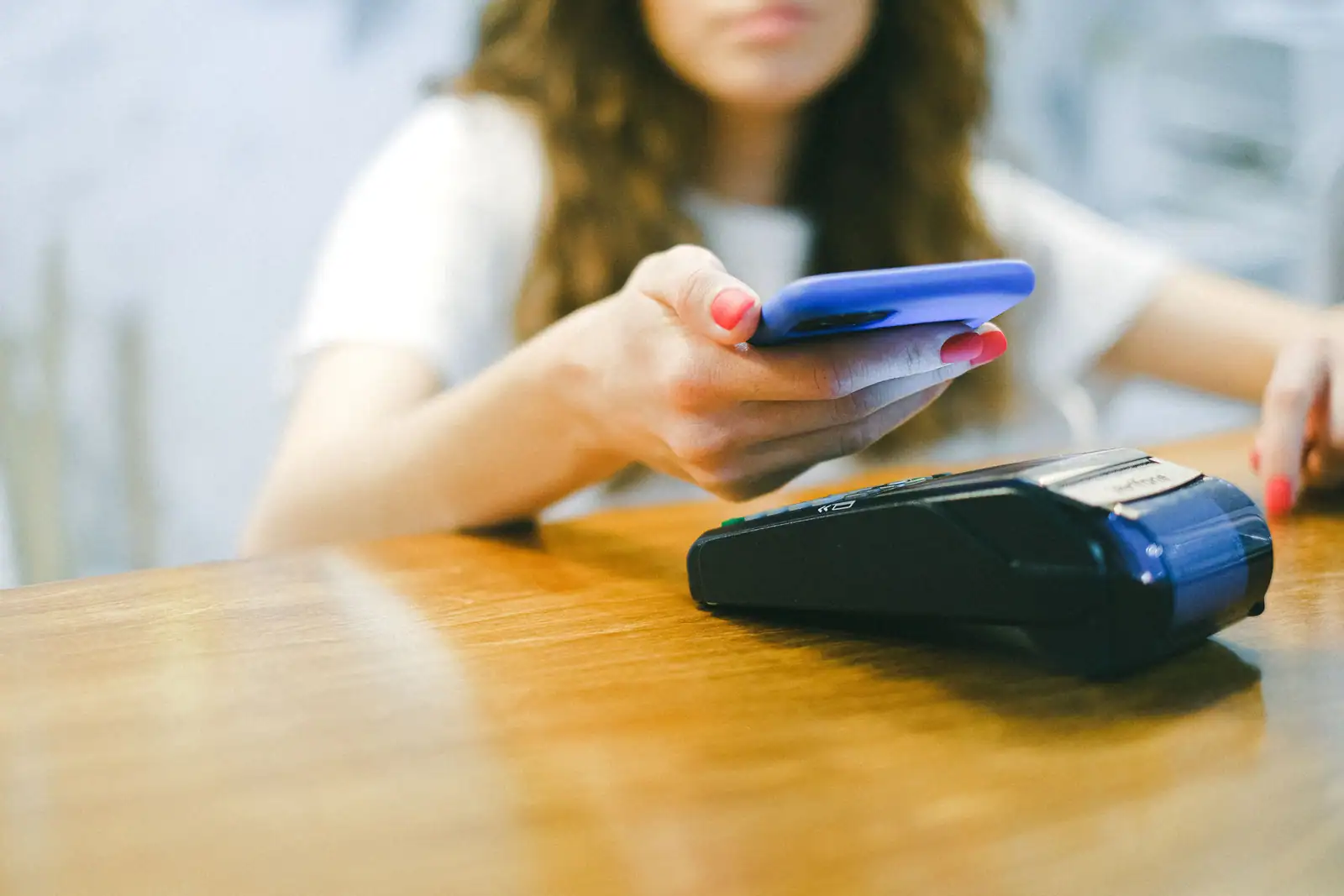 Femme approchant son téléphone d’un terminal de paiement posé sur une table, pour régler sans contact