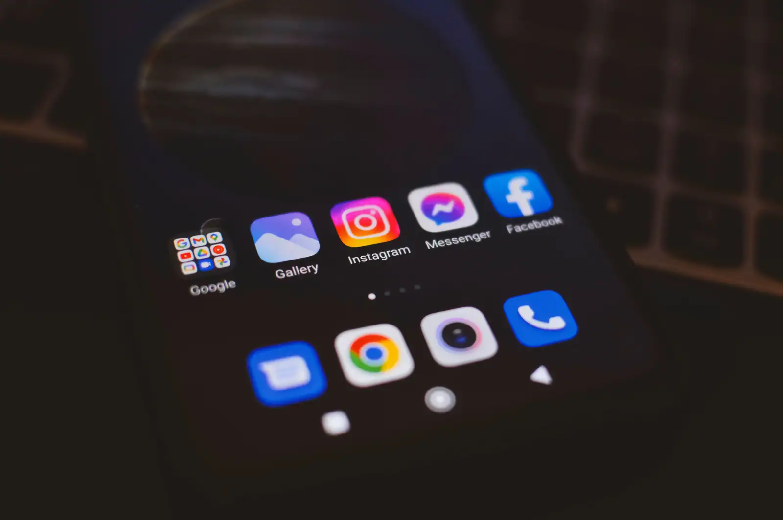 Écran d'accueil d'un smartphone posé sur un clavier d'ordinateur, montrant plusieurs icônes d'applications.