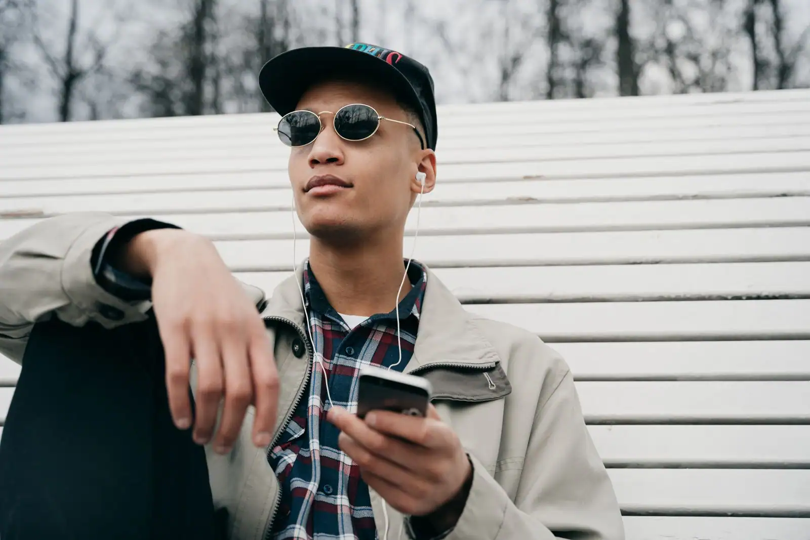 Homme assis en extérieur, écouteurs filaires aux oreilles et smartphone tenu à la main pendant son écoute.