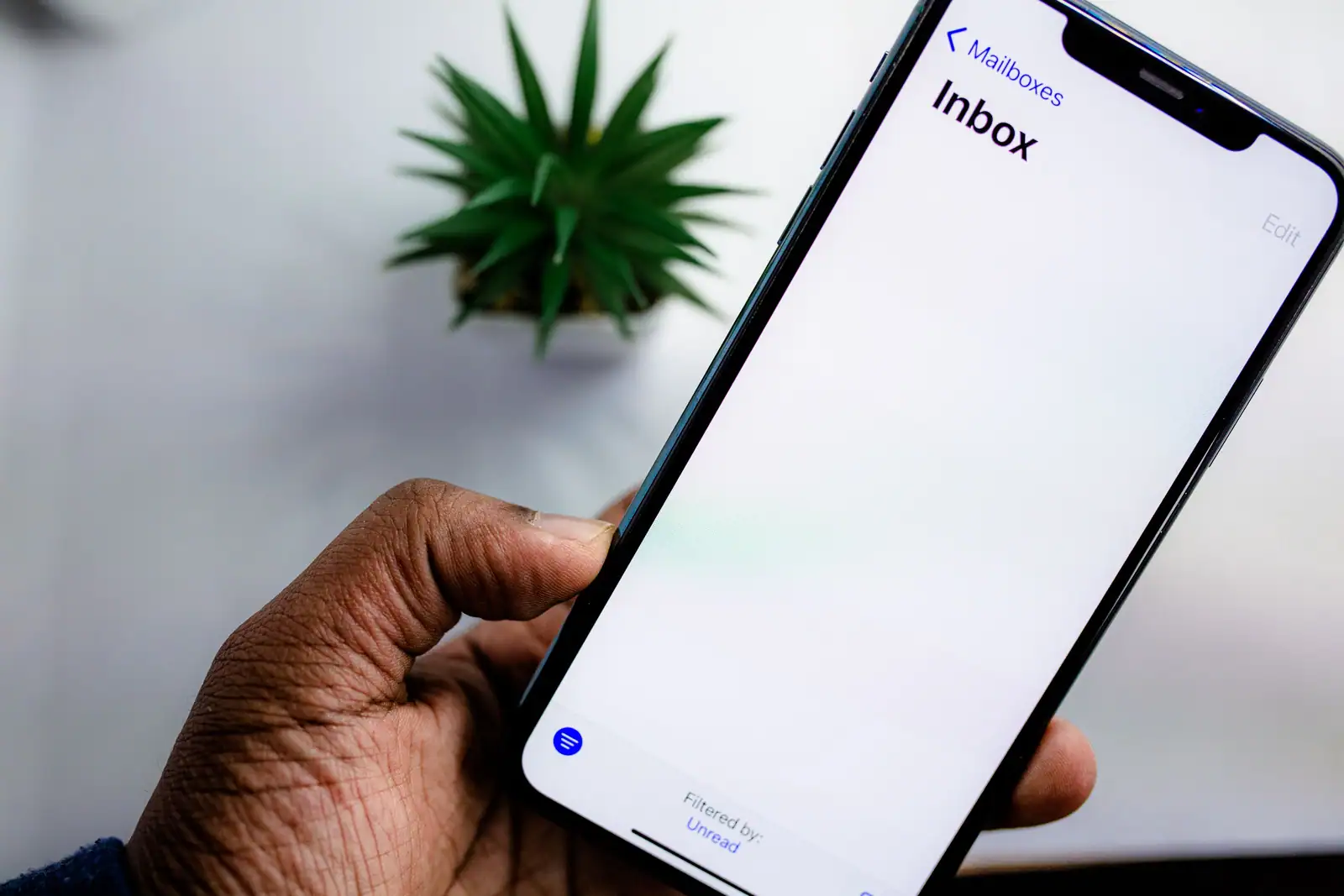 Main tenant un smartphone dont l'écran affiche la boîte de réception d'une application de messagerie