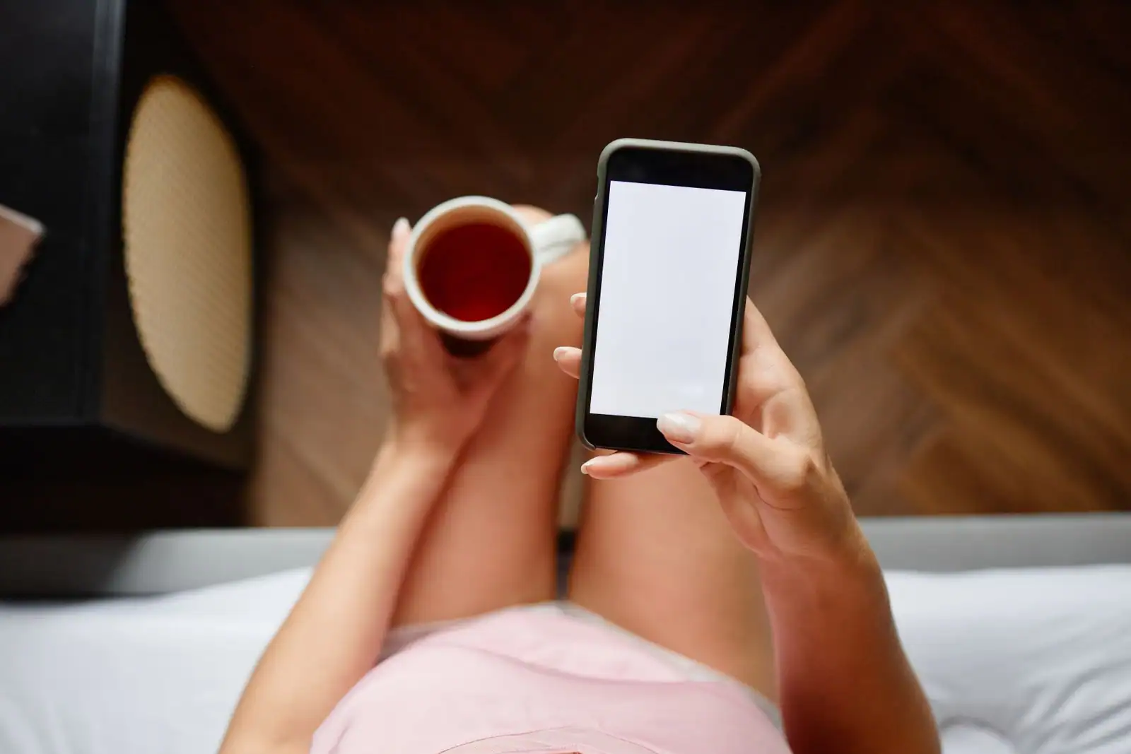 Personne allongée tenant son smartphone en mode portrait, une tasse à la main, dans une ambiance de lecture détendue.