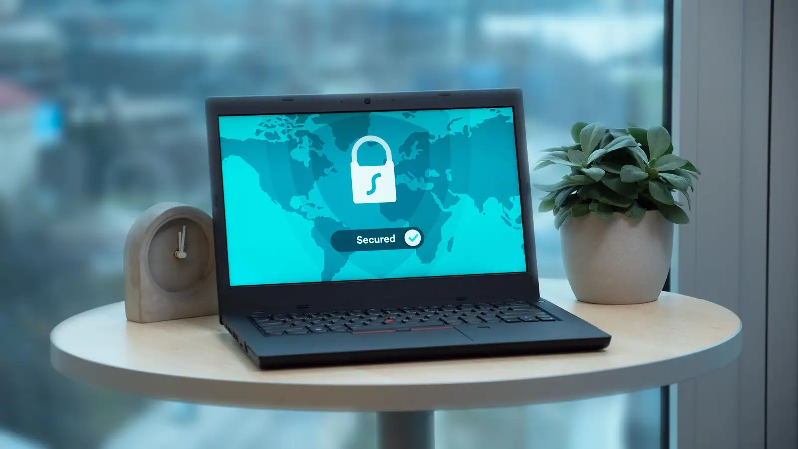 Ordinateur portable posé sur une table ronde, écran affichant un grand cadenas blanc et la mention « Secured ».