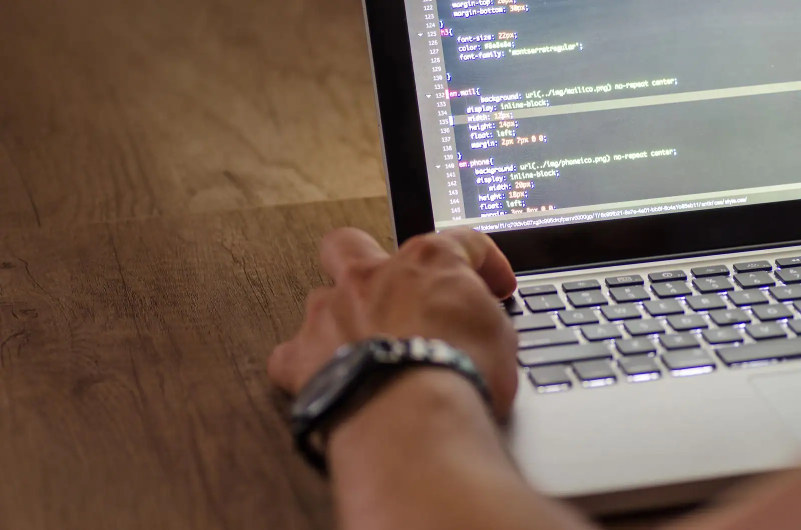 Main sur le clavier d'un ordinateur portable affichant du code à l'écran, en situation de développement.