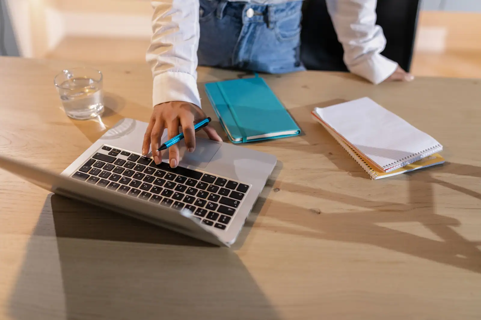 Personne installée à un bureau clair, la main sur un ordinateur portable ouvert, carnets à côté