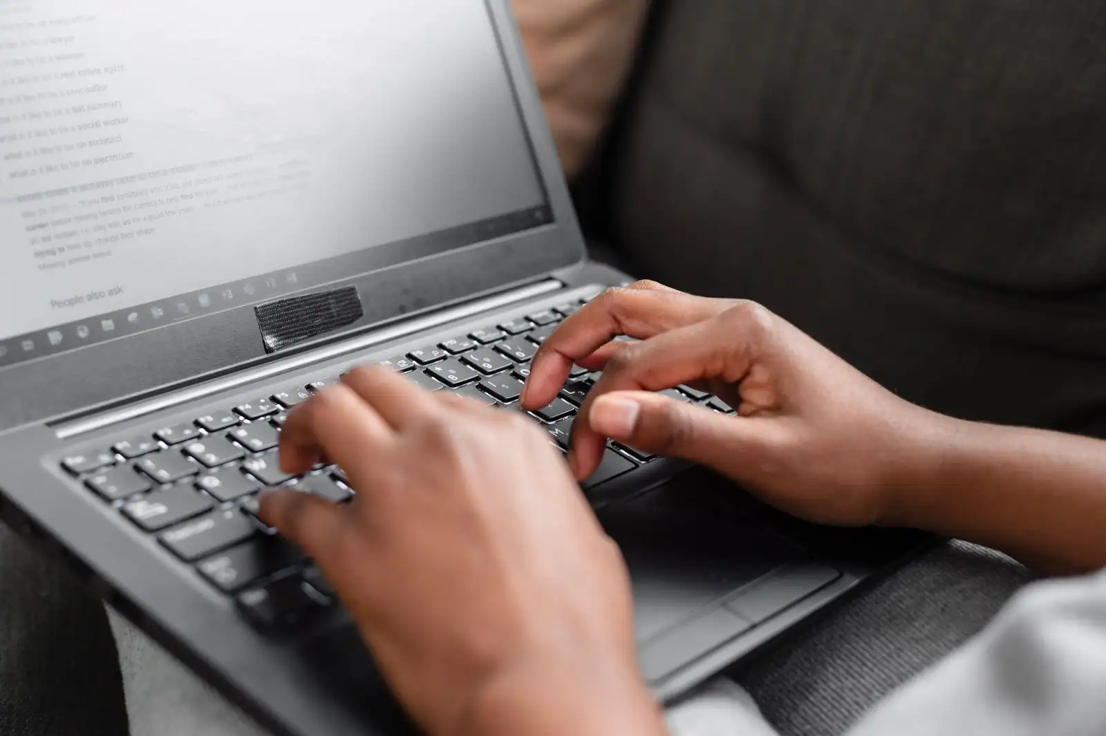 Mains posées sur le clavier d’un ordinateur portable en train d’écrire, écran de texte affiché