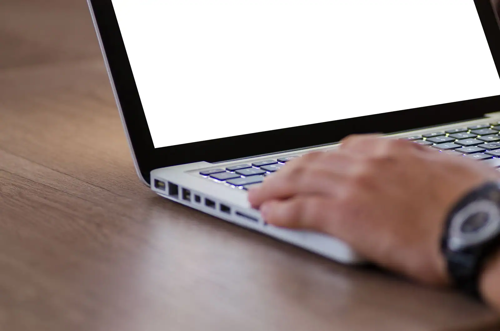 Mains d'une personne tapant sur le clavier d'un ordinateur portable posé sur un bureau en bois