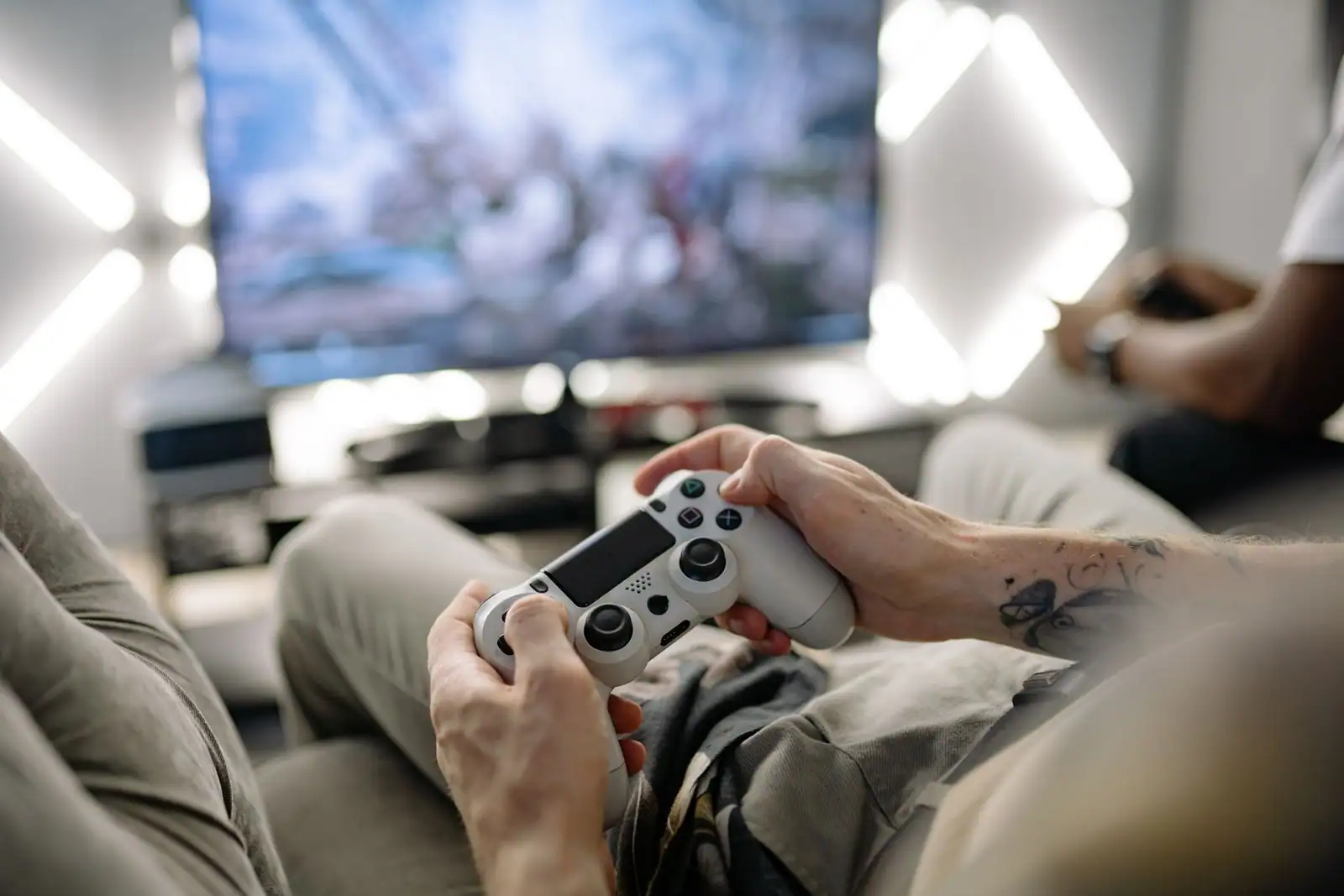 Manette de jeu sans fil tenue à deux mains dans un canapé, face à un téléviseur qui affiche un jeu.