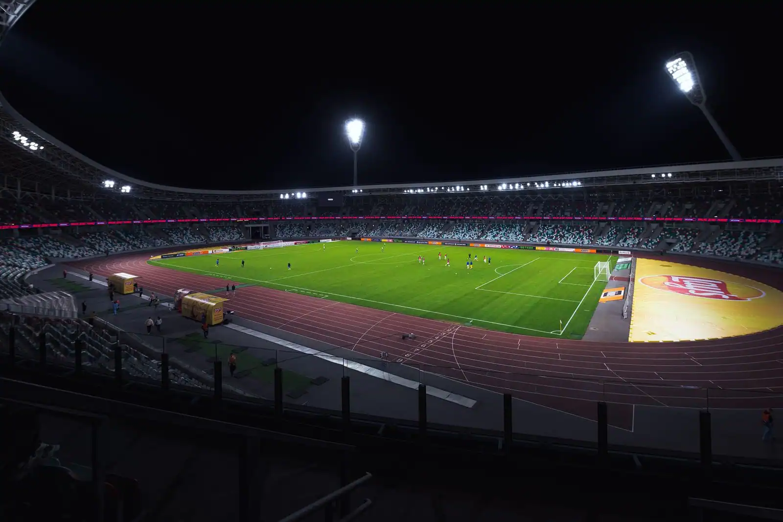 Stade de football illuminé par les projecteurs la nuit, avec sa pelouse verte et ses gradins