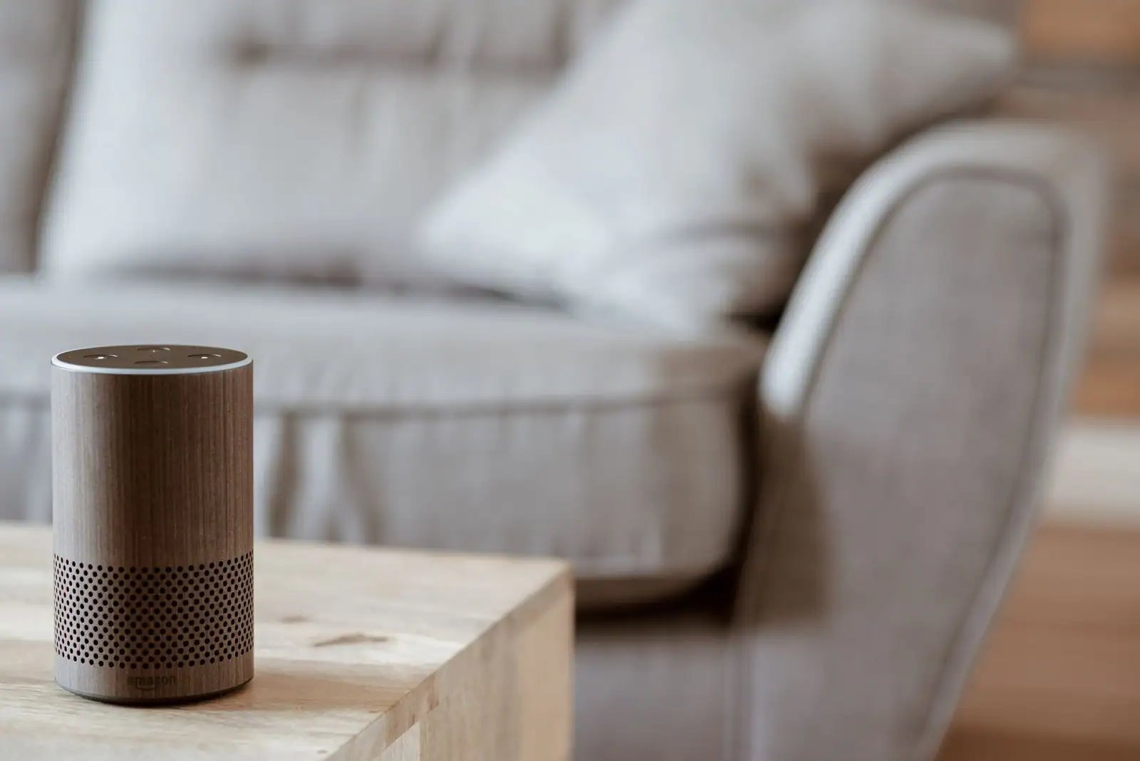 Enceinte connectée en habillage bois posée sur une table basse, devant un canapé clair dans un salon.