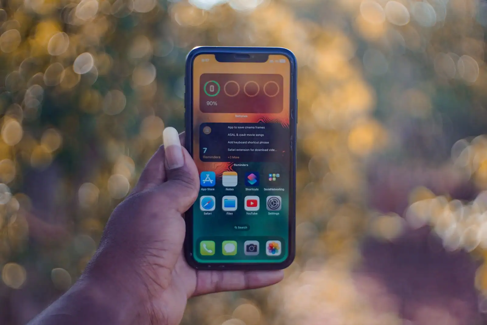 Main tenant un smartphone affichant son écran d'accueil et ses applications.