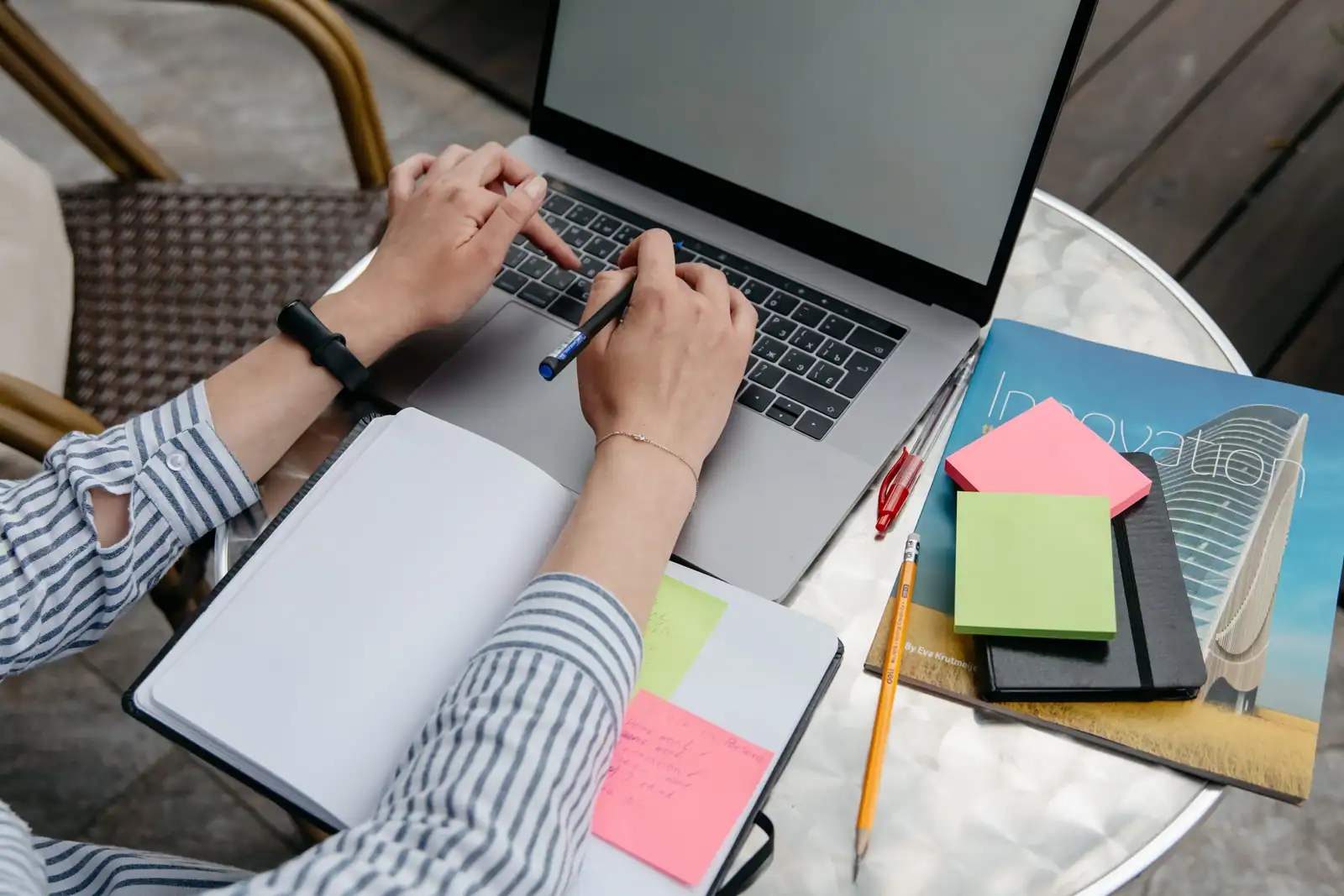 Vue plongeante sur des mains posées sur le clavier d’un ordinateur portable, à côté d’un carnet ouvert.