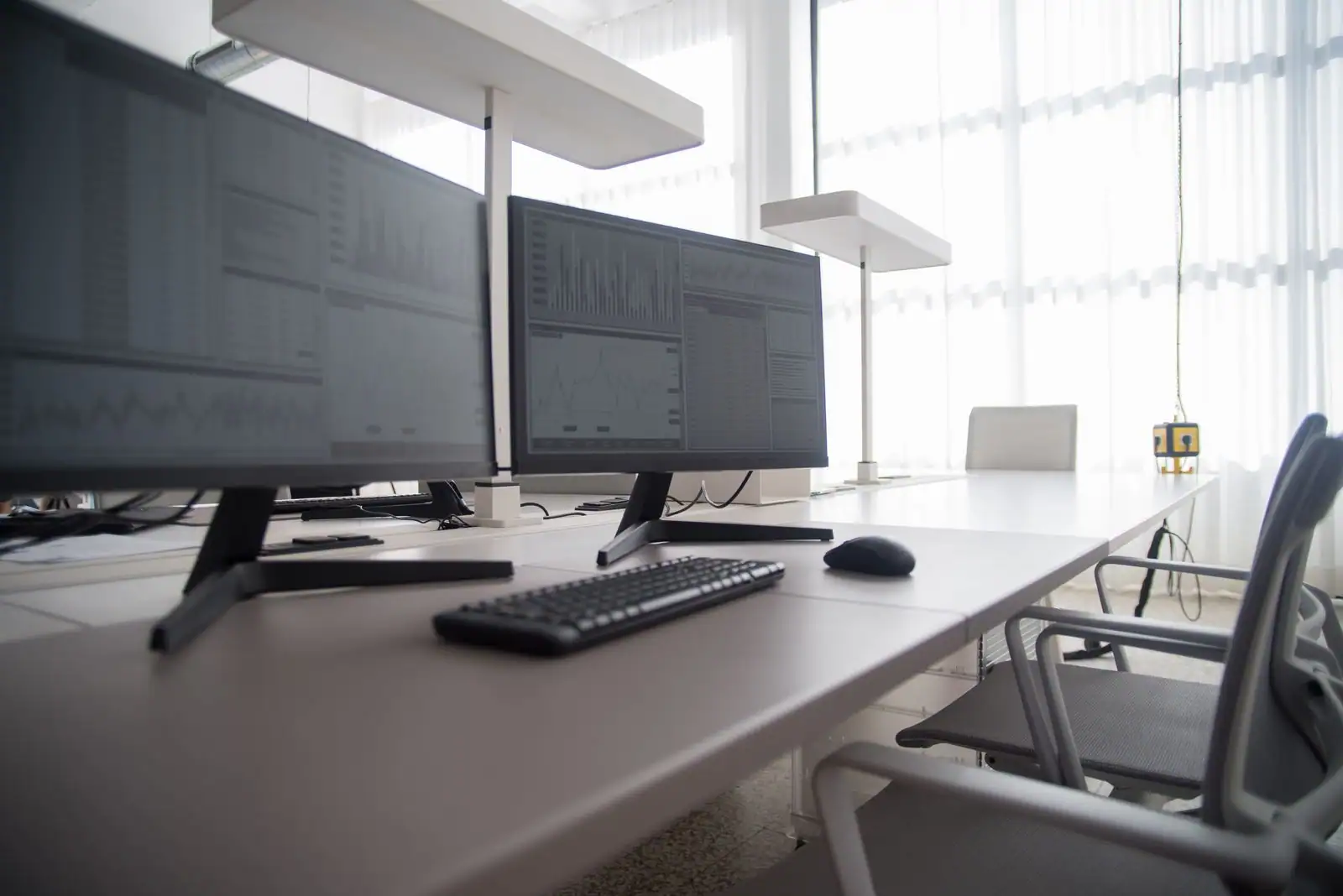 Deux écrans d'ordinateur affichant des graphiques, avec clavier et souris, sur un bureau blanc lumineux