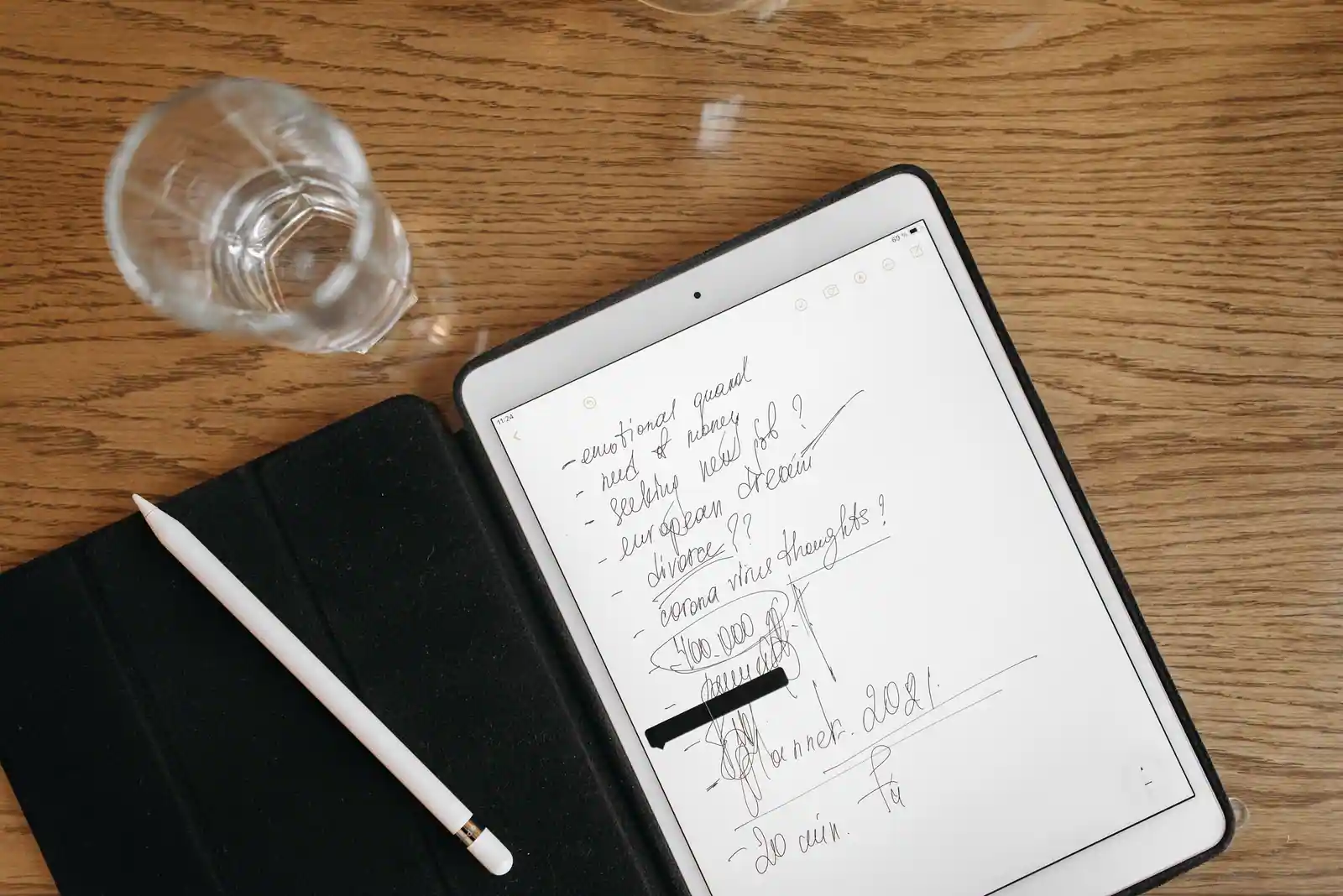 Tablette dans son étui posée sur une table en bois, stylet blanc à côté et notes manuscrites à l'écran