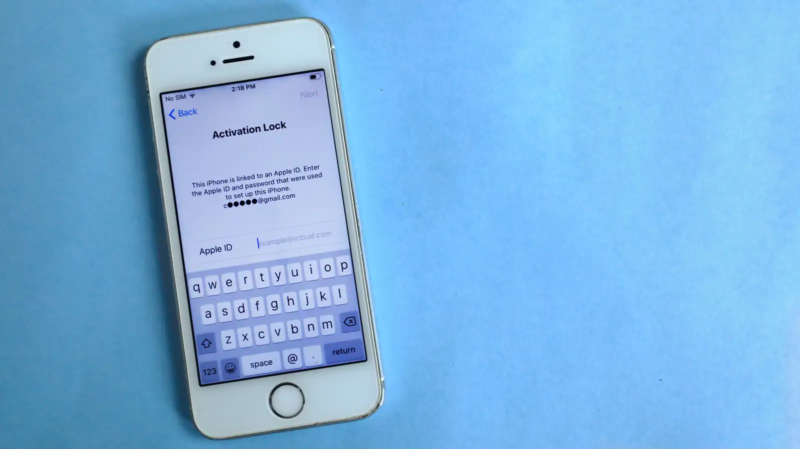 Un iPhone posé sur un fond bleu uni affiche l'écran de verrouillage d'activation qui réclame un identifiant Apple.