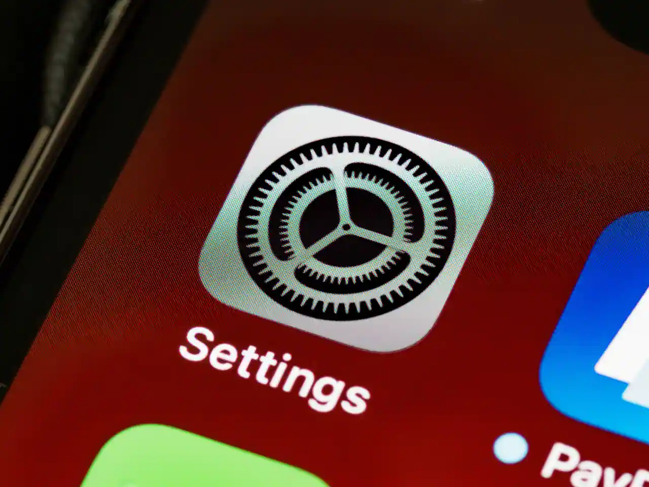Gros plan sur l'icône Réglages d'un iPhone : une roue dentée grise sur l'écran d'accueil.