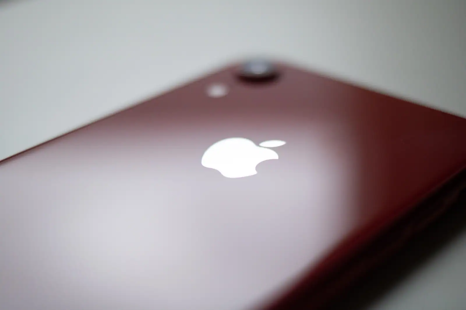 Dos en verre rouge d'un iPhone posé sur une surface claire, avec son capteur photo unique.