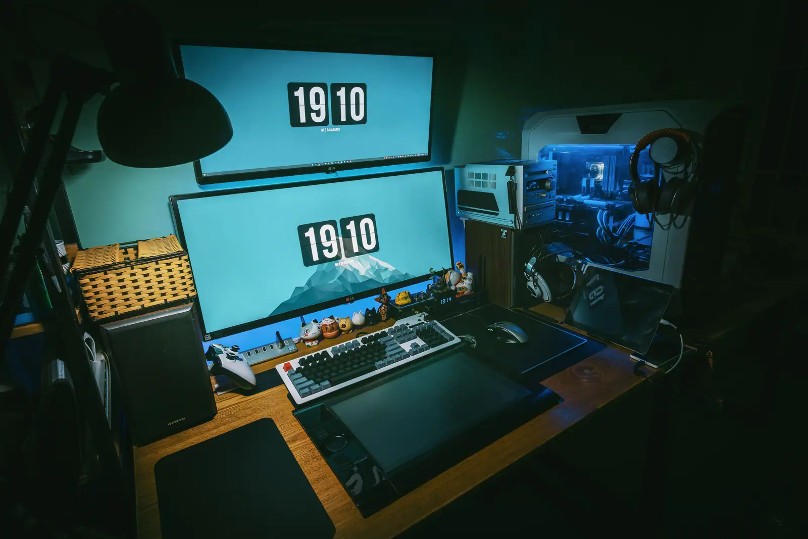 Bureau de jeu sur PC dans la pénombre : tour vitrée éclairée en bleu, double écran, clavier et casque