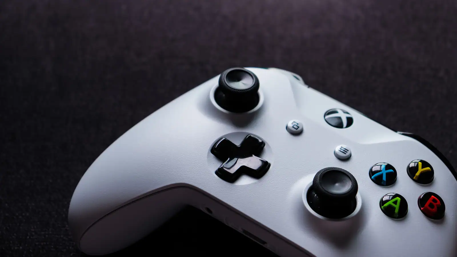 Gros plan sur une manette Xbox blanche posée sur un tissu sombre, boutons colorés ABXY bien visibles.