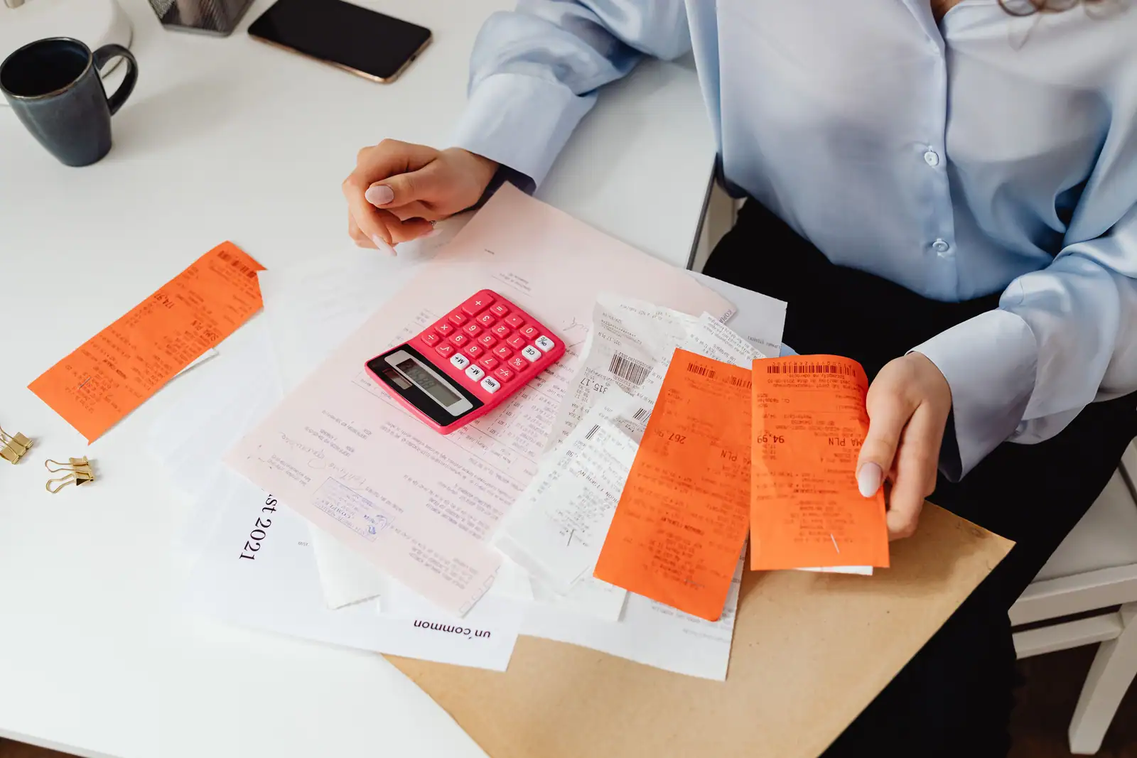 Personne assise à un bureau tenant des tickets de caisse, avec une calculatrice et une pile de justificatifs