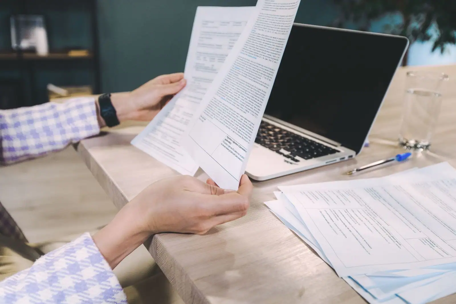 Personne examinant des documents administratifs à un bureau, un ordinateur portable ouvert à côté.