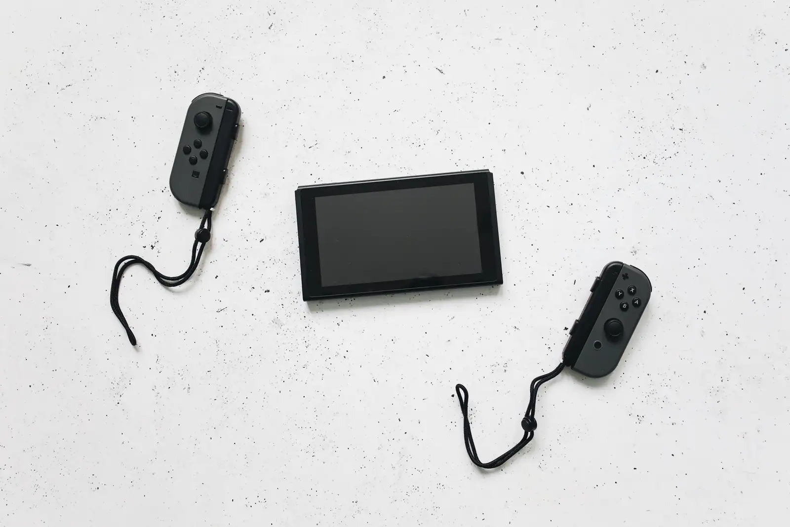 Console Nintendo Switch à écran éteint posée à plat, ses deux manettes détachées de part et d'autre